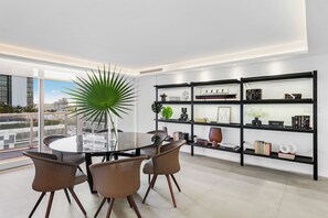 A modern dining area with a round glass table, four brown chairs, and a large potted plant.
