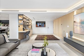 Un salon moderne comprenant un canapé, une table basse avec des livres et un vase, un coin repas avec des chaises et une table, et une cuisine avec des étagères et un téléviseur.