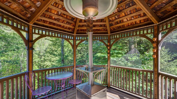 A covered wooden deck with a central heater, a table, and two chairs. - Charming Thornton Escape w/ Sauna + Gazebo! (Thornton)
