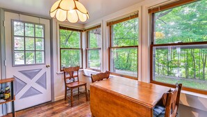 Una habitación con una mesa de madera, dos sillas, un banco y un ventanal grande con vistas a un bosque.