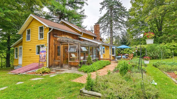 Una casa de madera amarilla con un porche cubierto y un jardín.