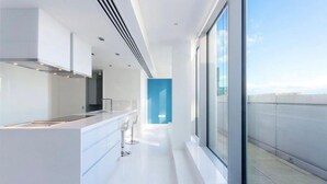 Une cuisine moderne dotée d’un îlot central, de meubles blancs et offrant une vue sur la ville grâce à de grandes fenêtres.