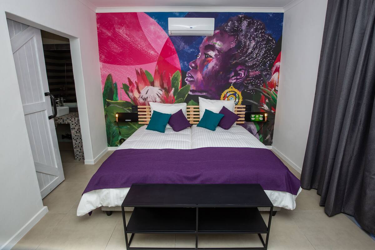 A bedroom with a bed, a bench, a wall mural, and a door.