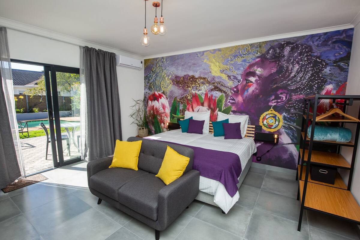A modern bedroom with a bed, a sofa, and a mural on the wall.