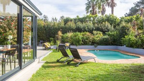 A modern outdoor pool area with lounge chairs, a dining table, and a glass-enclosed patio. - Casa iLanga guesthouse (Cape Town)