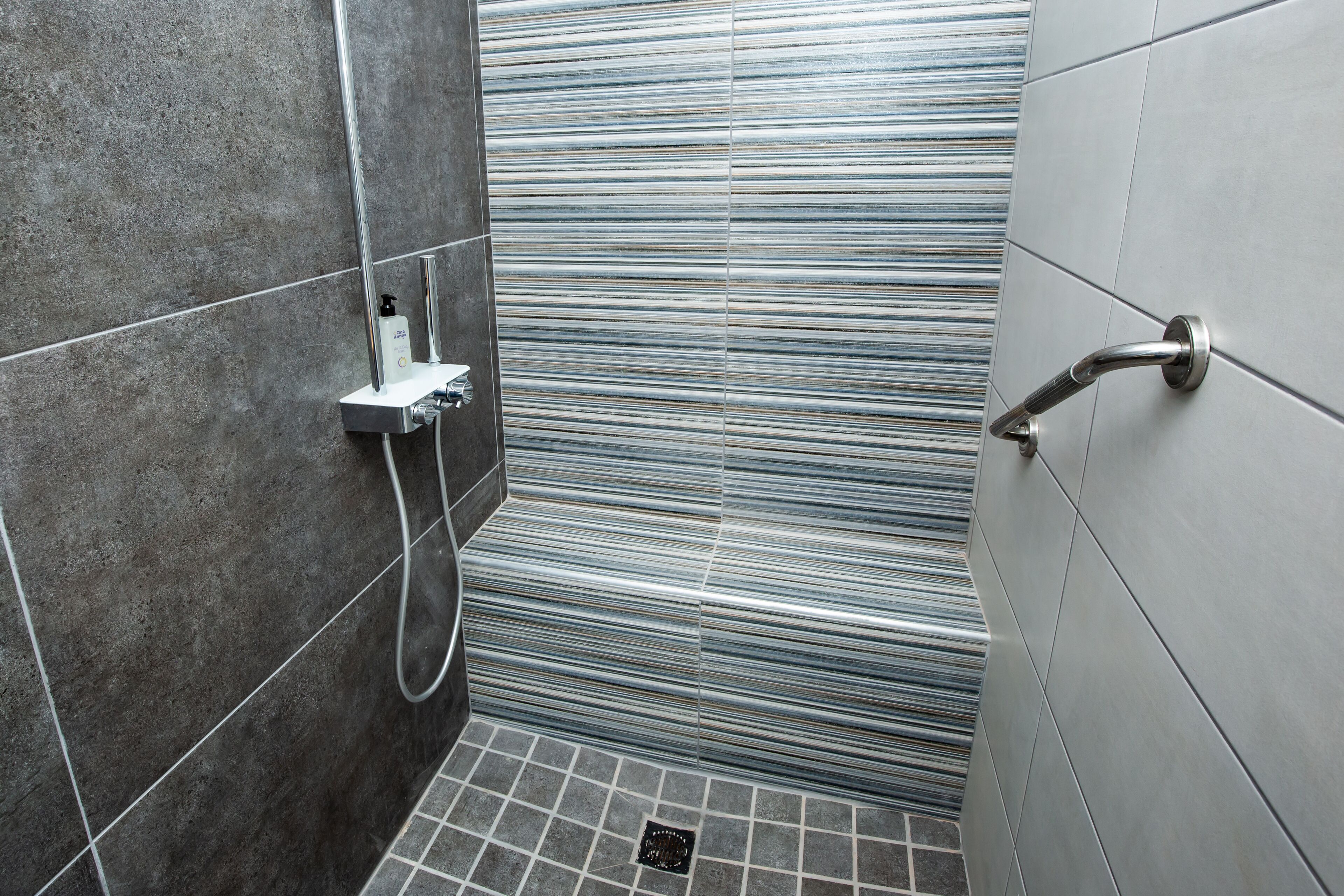 Un espace douche avec un mur carrelé, une douchette à main et un panneau de commande de la douche.