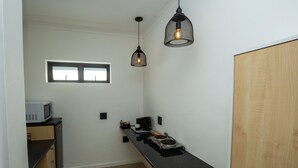 A compact kitchen with a microwave, coffee maker, and a small countertop. There are two pendant lights and a window above the sink. - Casa iLanga guesthouse (Cape Town)