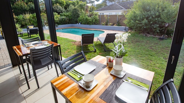 A dining area with a view of a backyard, including a swimming pool and greenery. - Casa iLanga guesthouse (Cape Town)