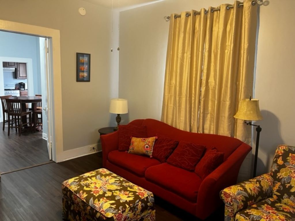 A living room with a red sofa, a floral ottoman, and a yellow curtain.