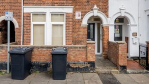 A two-story brick house with a white front door, two windows with shutters, and a small porch area. - Studio Flat in Bedford Near Hospital & Stations (Bedford)