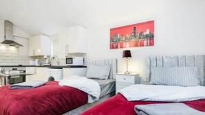 A modern hotel room with two beds, a kitchenette, a cityscape painting, and a city skyline view. - Studio Flat in Bedford Near Hospital & Stations (Bedford)