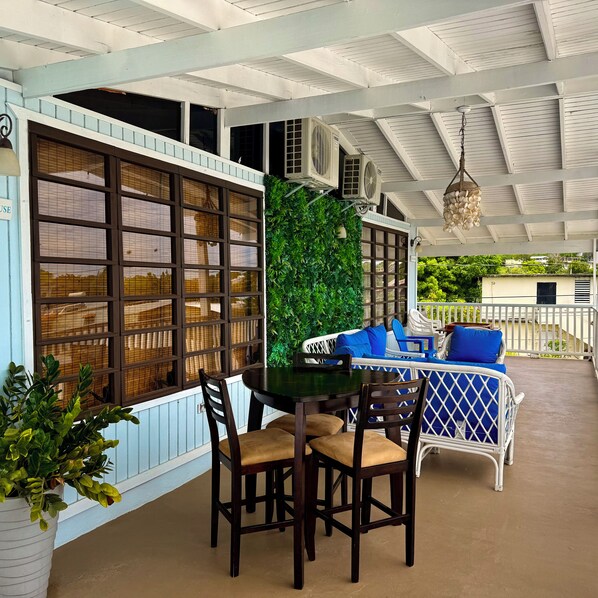 A covered patio area with a table and chairs, a white outdoor sofa with blue cushions, and a green vertical garden.