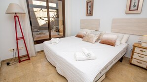 Un lit bien fait, recouvert d’une couette blanche, une lampe de sol rouge et une table de chevet en bois avec une lampe.