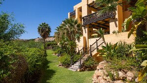 Un bâtiment doté d’un escalier en pierre menant à un balcon, entouré d’une végétation luxuriante et de palmiers.