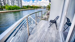 Ein Balkon mit Geländer, der auf einen Fluss blickt, mit einem Stuhl und einem kleinen Tisch.
