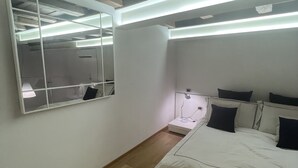 Une chambre à coucher comprenant un lit, un miroir, une table de chevet et un plafond avec des poutres apparentes.