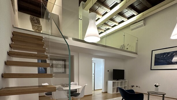 Un intérieur moderne avec un escalier en bois, un coin repas avec des chaises blanches, un canapé noir et un sol en marbre.