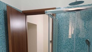 Une salle de bain avec une douche à parois de verre, une porte en bois et un sol carrelé.