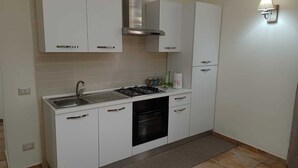 Une cuisine compacte avec des meubles blancs, un évier en acier inoxydable, une cuisinière à gaz et un four encastré.