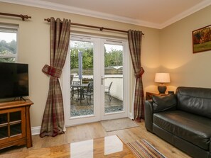 A living room with a TV, a leather sofa, a lamp, and a sliding glass door leading to an outdoor patio with a table and chairs. - Castle Crag (Keswick)