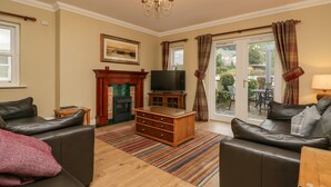 A living room with a fireplace, leather sofas, a TV, and a large window with curtains. - Castle Crag (Keswick)