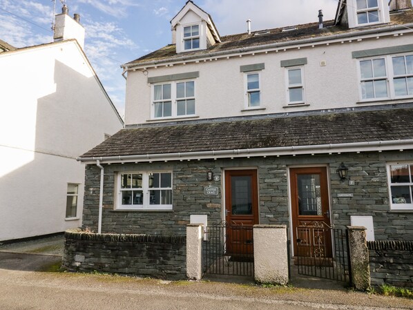A two-story stone house with a stone facade, a wooden door, and a small porch with a stone wall and metal gate. - Castle Crag (Keswick)