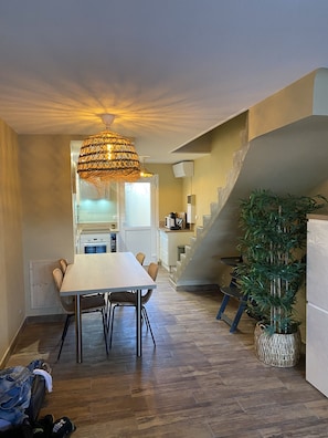 Uma área de refeições com mesa e cadeiras, luminária pendente, escada e planta em vaso.