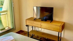 Ein Hotelzimmer mit einem Bett, einem hölzernen Schreibtisch mit Fernseher und einem Fenster mit Jalousien.