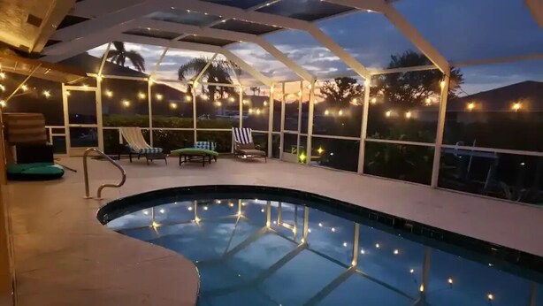 An indoor swimming pool with a glass ceiling, string lights, and lounge chairs. - Tropical Breeze  Heated Pool, Canal Home, King bed. (Cape Coral)