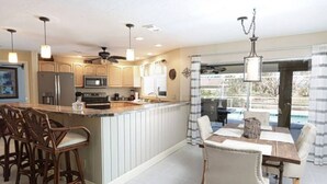 A kitchen with a central island, bar stools, and a dining area with a table and chairs. - Tropical Breeze  Heated Pool, Canal Home, King bed. (Cape Coral)