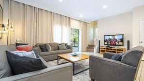 A modern living room with a sofa, armchair, and coffee table, a flat-screen TV, and a wooden entertainment unit.