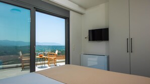 Une chambre avec un lit, un téléviseur fixé au mur, un balcon avec une table et des chaises, et une vue sur la ville et les montagnes.