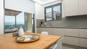 Une cuisine moderne avec une grande fenêtre, une table à manger sur laquelle se trouve un saladier rempli de nourriture, et une vue sur l’extérieur.