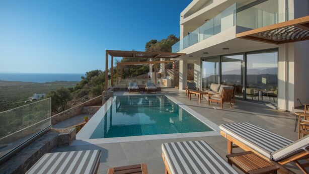 Un espace piscine extérieur moderne, doté de chaises longues, d’une pergola et offrant une vue sur la mer.