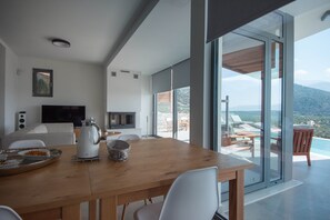 Une cuisine moderne avec une table en bois, des chaises blanches et une grande fenêtre donnant sur un paysage magnifique.