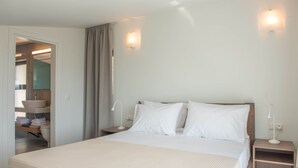 Ein Hotelzimmer mit einem großen Bett, Nachttischen, einer Nachttischlampe und einem durch eine offene Tür einsehbaren Badezimmer.