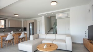 Ein moderner Wohnraum mit einem Ecksofa, einem Esstisch mit Stühlen, einem runden Couchtisch und einem Fernseher auf einem Holzgestell.