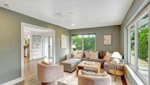 A spacious living room with a grey sofa set, a coffee table, and a large window offering a view of greenery. - ~NEW~Casa Miami~Luxury Oasis w/ Pool&Game Paradise (Miami)