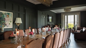 Une salle à manger élégante, avec une longue table dressée pour un repas, entourée de chaises.