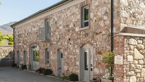 Un bâtiment en pierre doté de nombreuses portes et fenêtres, un petit jardin agrémenté de plantes et de fleurs, et un panneau indiquant qu’un espace repas est réservé uniquement à la cour.