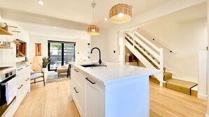 A modern kitchen with white cabinetry, a central island, and a staircase leading to an upper level.