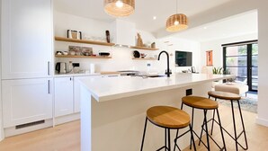A modern kitchen with white cabinetry, a large island with stools, pendant lighting, and a view to the outside.