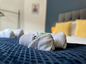 A neatly made bed with a blue textured bedspread, a rolled-up towel with a logo, and a pillow with a yellow cover. - Stylish Terrace with Free Parking - Pass the Keys (Blyth)