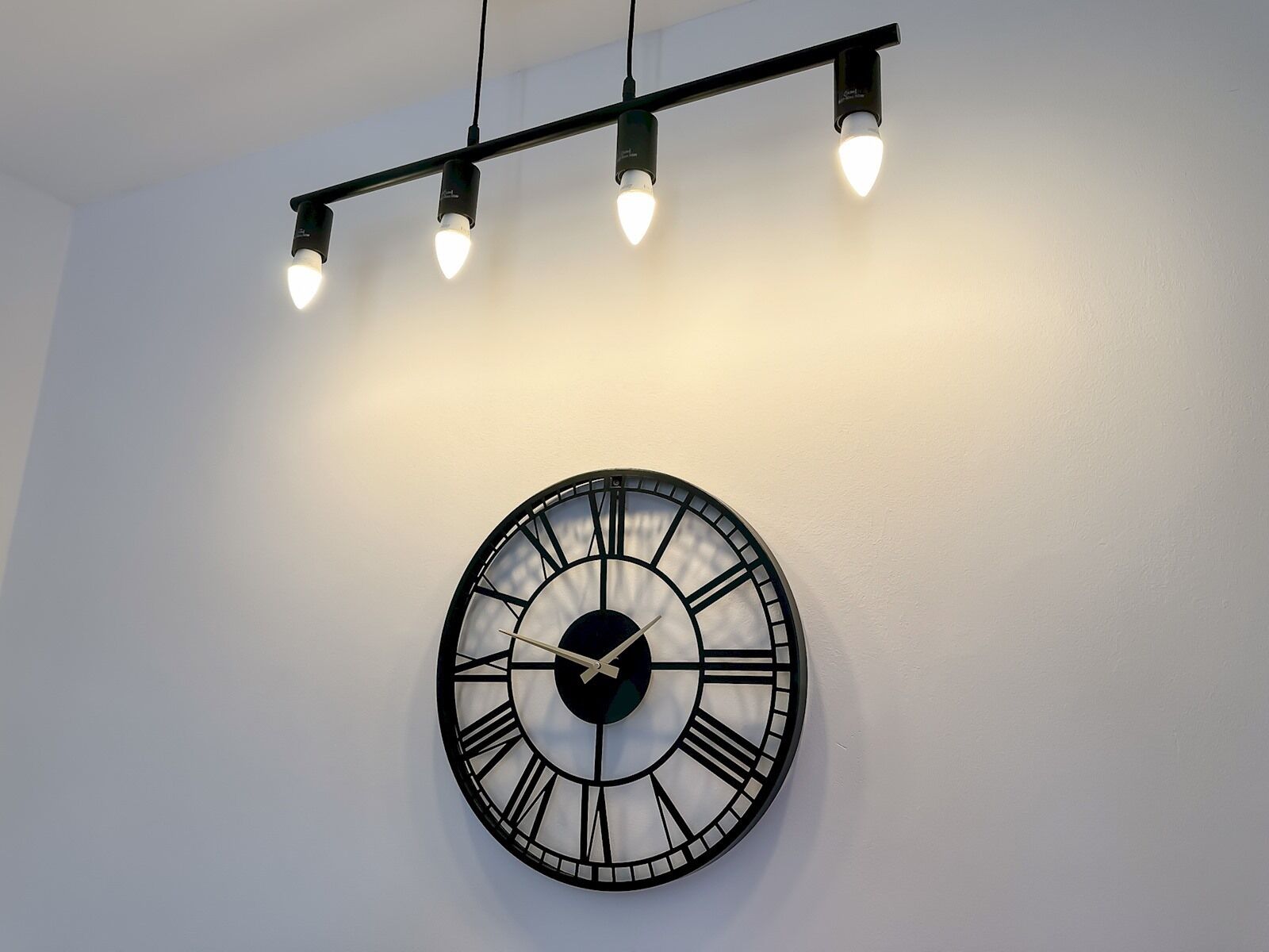 A wall-mounted clock with Roman numerals and a modern light fixture above it.
