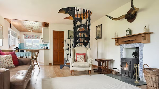 A cozy living room with a fireplace, a spiral staircase, and a dining area. - The Old Telephone Exchange Cartmel - Pass the Keys (Cartmel)