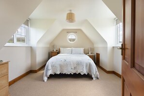 A bedroom with a sloped ceiling, a bed with a floral bedspread, a round wall clock, and a wooden dresser.