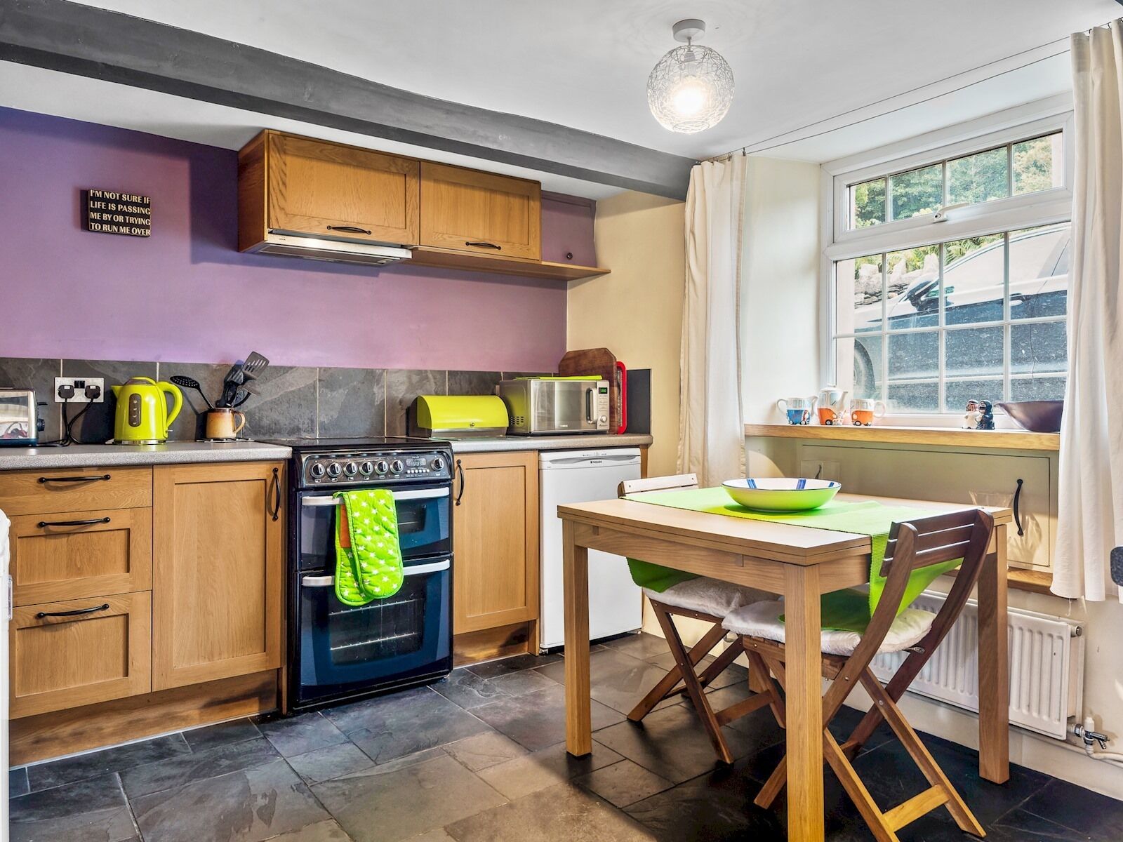 A kitchen with wooden cabinets, a stove, a microwave, and a window with a view.