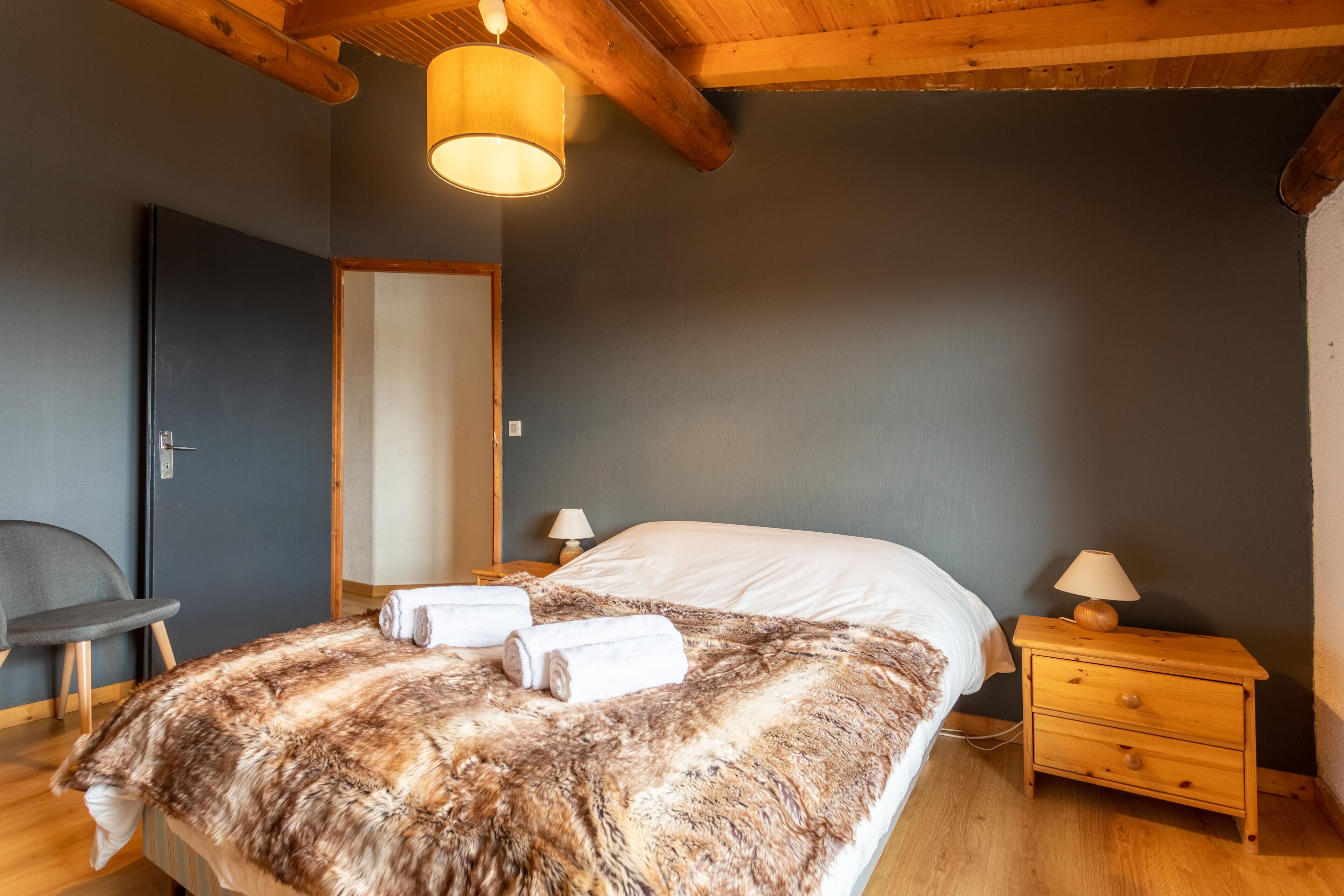 A bedroom with a large bed, wooden nightstand, and a chair.