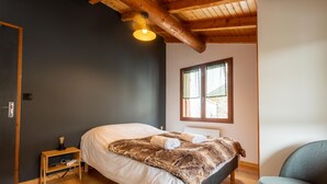 A bedroom with a bed, a wooden nightstand, a chair, a window, and a ceiling light. - Chalet “Le petit Paradis” in the heart of the 3 valleys! (Les Belleville)