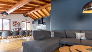 A modern living room with a sectional sofa, a round coffee table, and a dining area with chairs and a table. - Chalet “Le petit Paradis” in the heart of the 3 valleys! (Les Belleville)